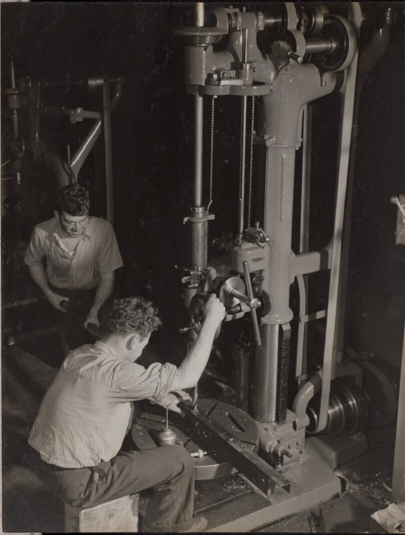 [Two men work with a large drill bit]