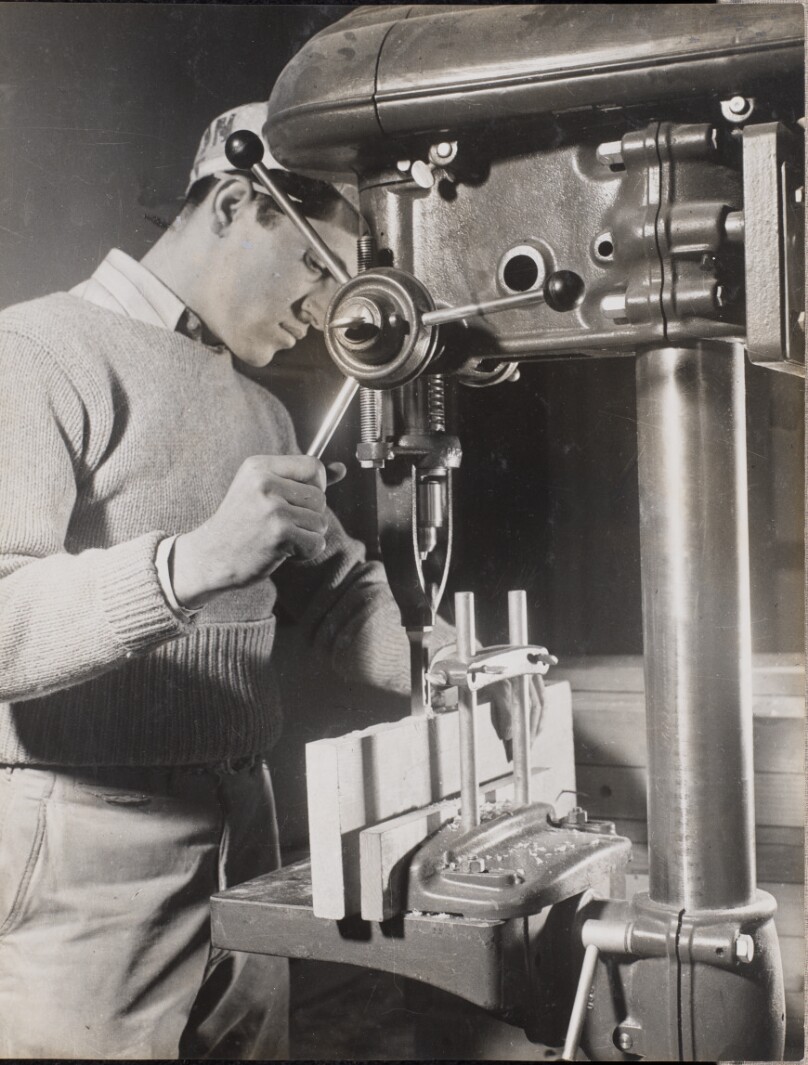 [Man uses a machine to drill holes in two wood blocks]
