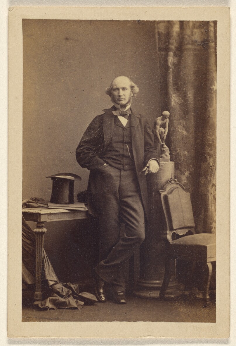 [Unidentified man standing, top hat on table]