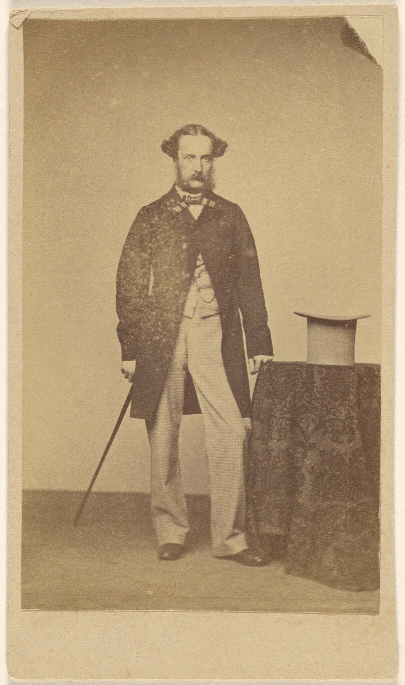 [Unidentified man with walking stick, standing near table with top hat]