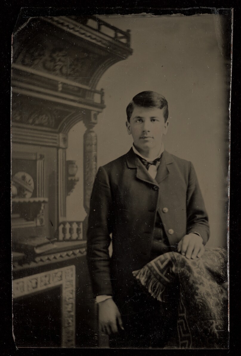 [Unidentified man standing, with one hand on a chair back]