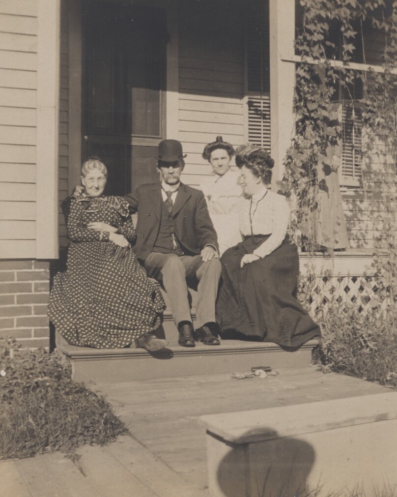 [Three women and a man in bowler seated on porch steps]