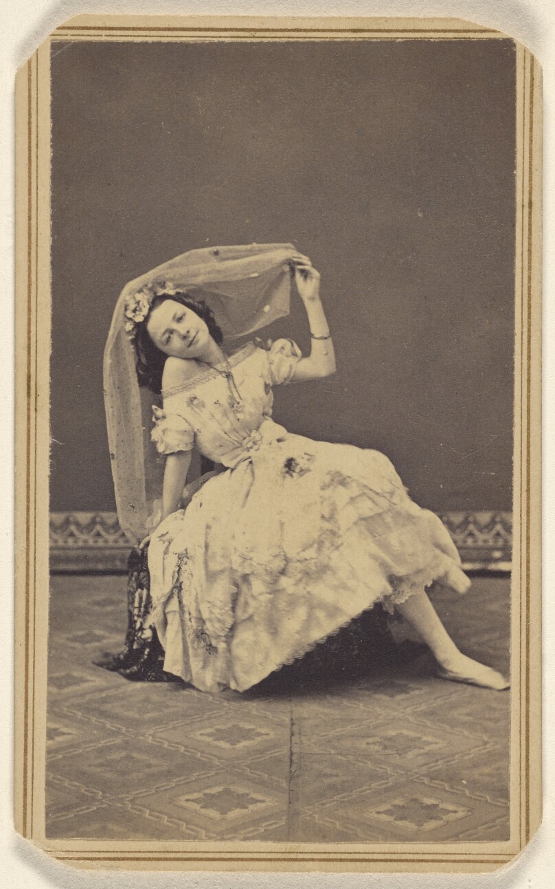 [Unidentified female dancer posed on a hassock wearing a veil on her head]