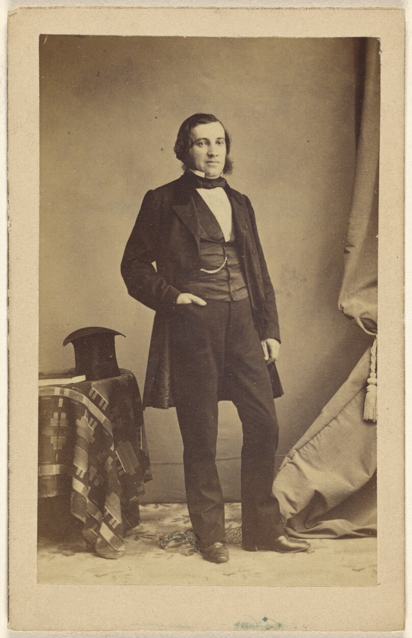 [Unidentified man standing with his hand in his pocket, a top hat on a table nearby]
