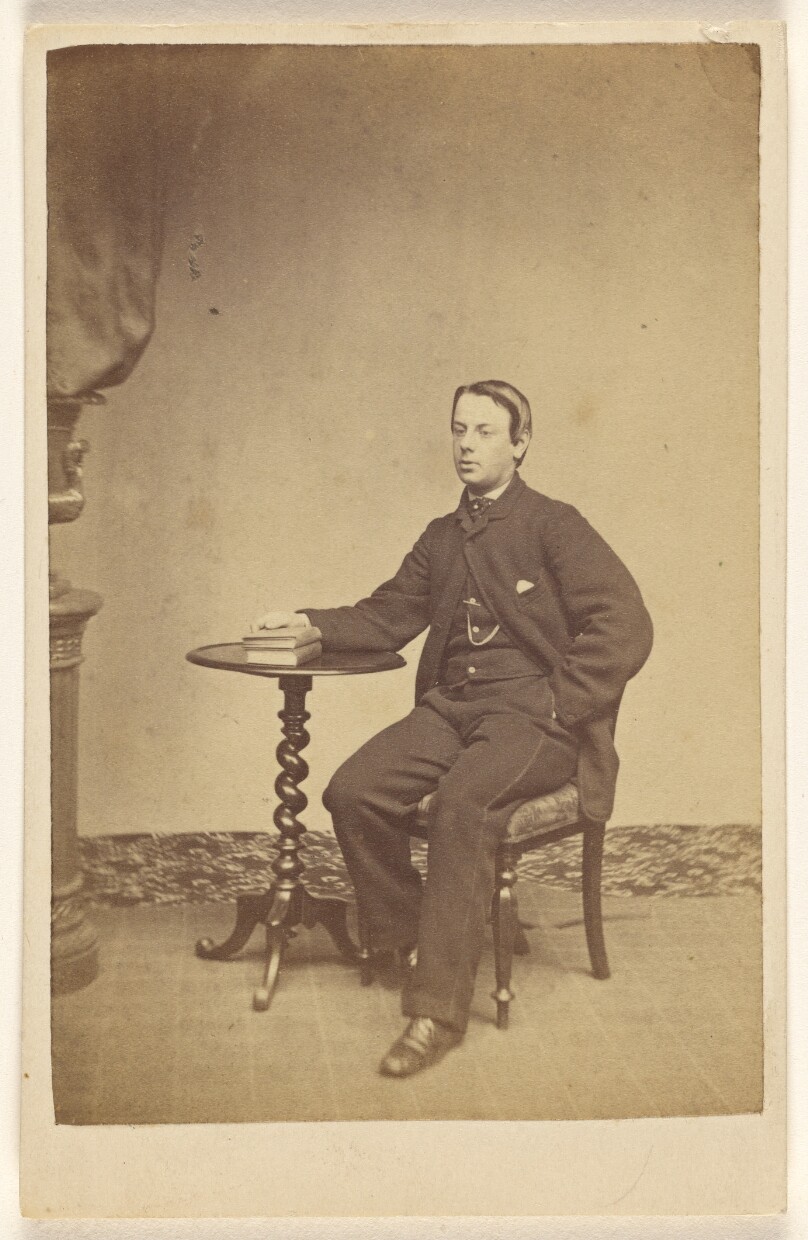 [Unidentified young man seated at a table with one hand on books]
