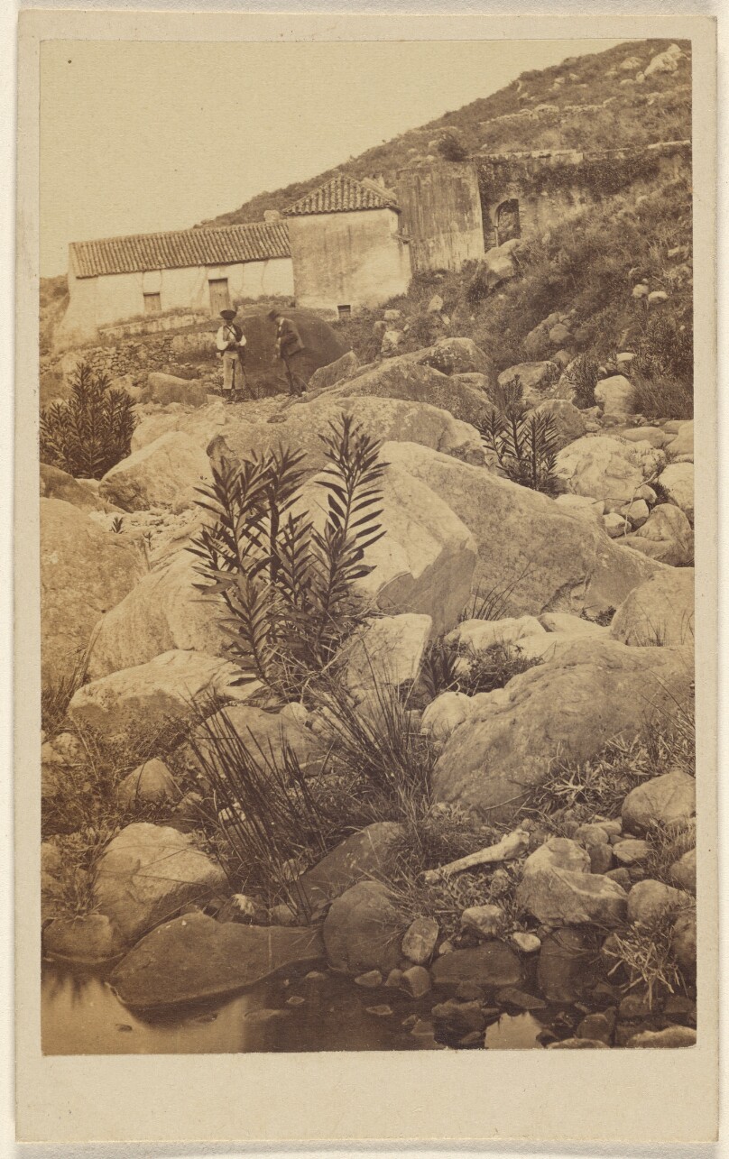 [Unidentified rocky landscape with two people and houses in the background]