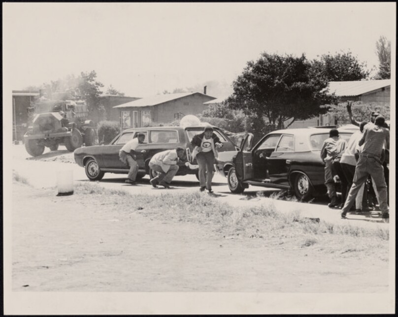 Untitled [Tank approaching street, men crouching by cars]