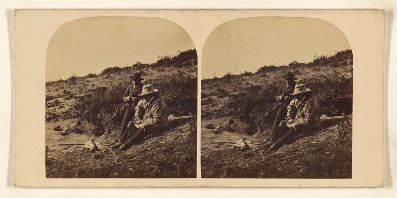 [Two men seated on ground, holding tools]