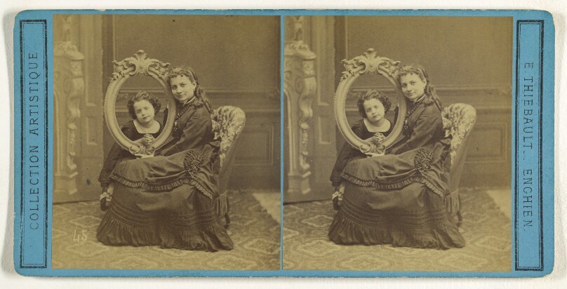 [Young woman posed with a child, the child's head is cutely being viewed through an empty picture frame]