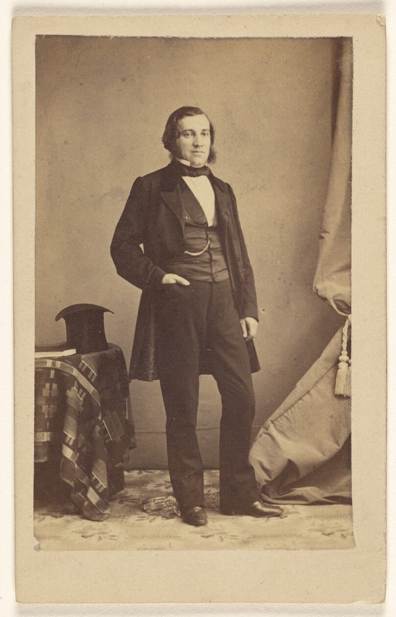 [Unidentified man with muttonchops, standing with his right hand in pocket, top hat on table]