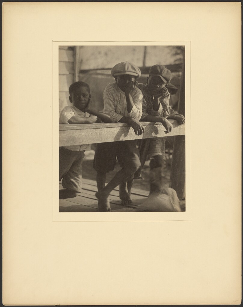 [Three Black Boys Leaning Over Wooden Railing]