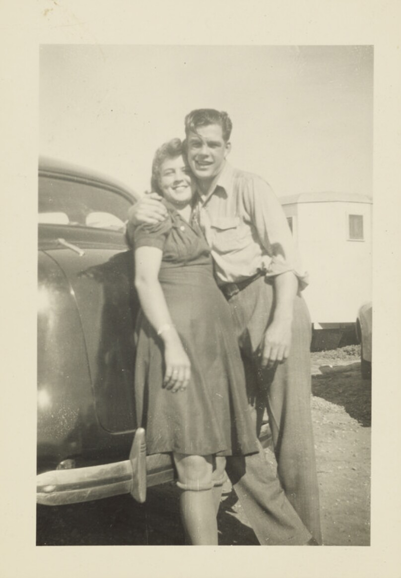 [Man embracing woman beside car]