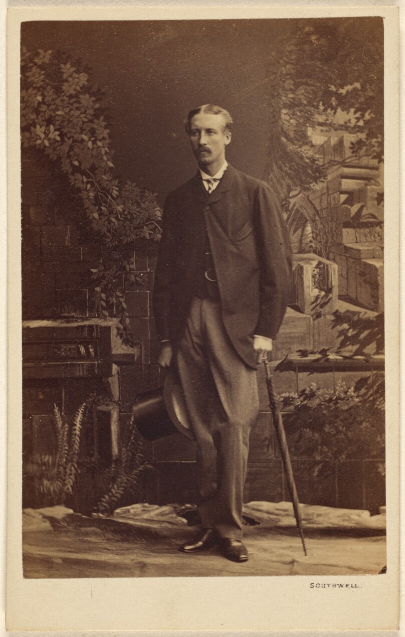 [Unidentified man with moustache, holding a top hat and umbrella, standing]
