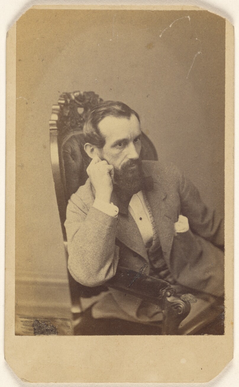 [Unidentified bearded man seated with right arm on chair arm, with hand to cheek]