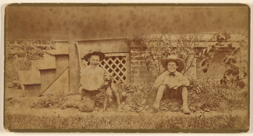[Two boys seated on ground with a dog]