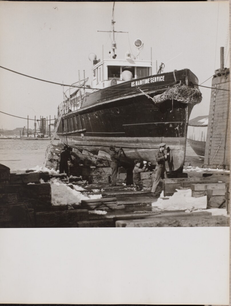 [Four men repair the lower half of a docked boat]