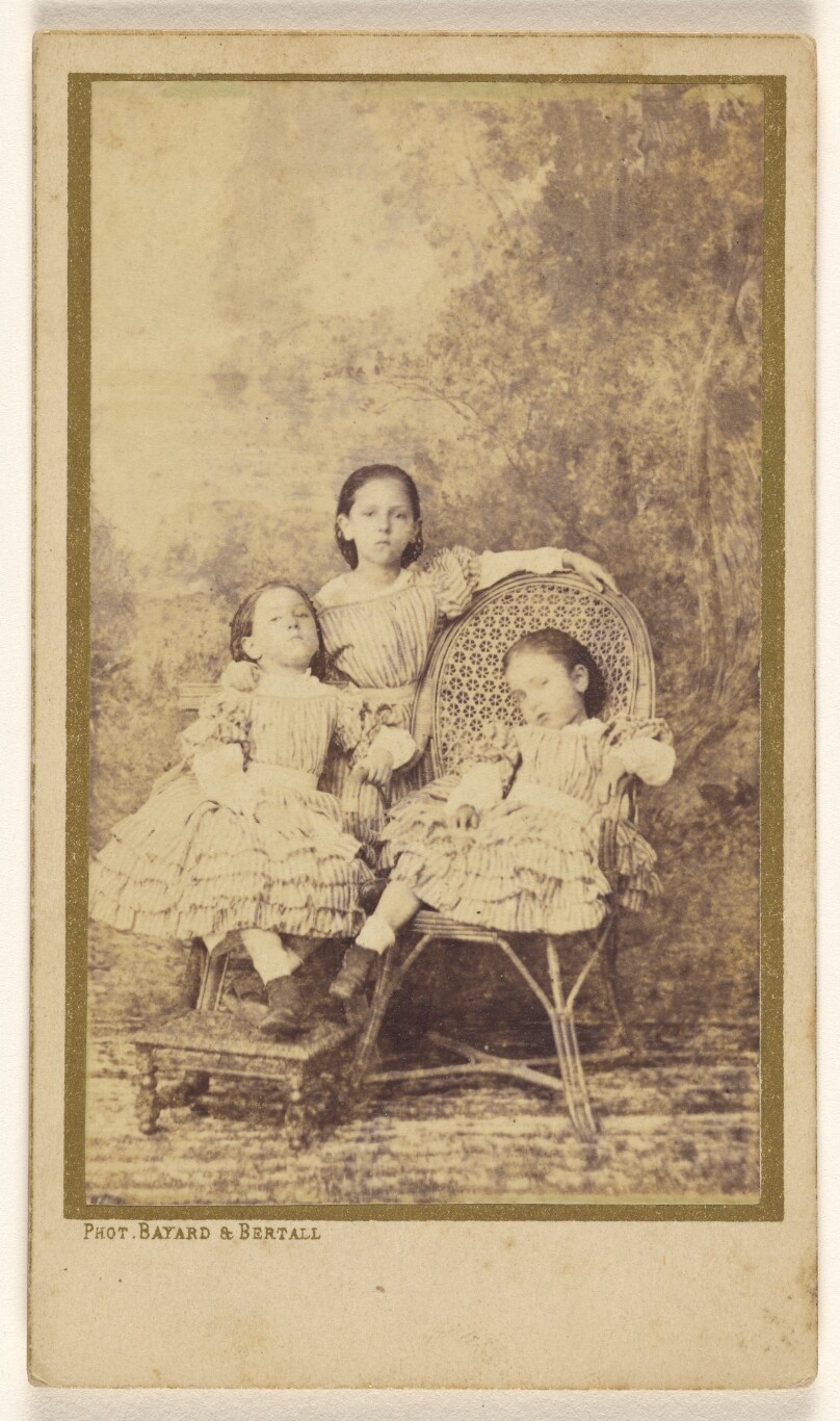 [Three little girls posed on chairs in a studio]