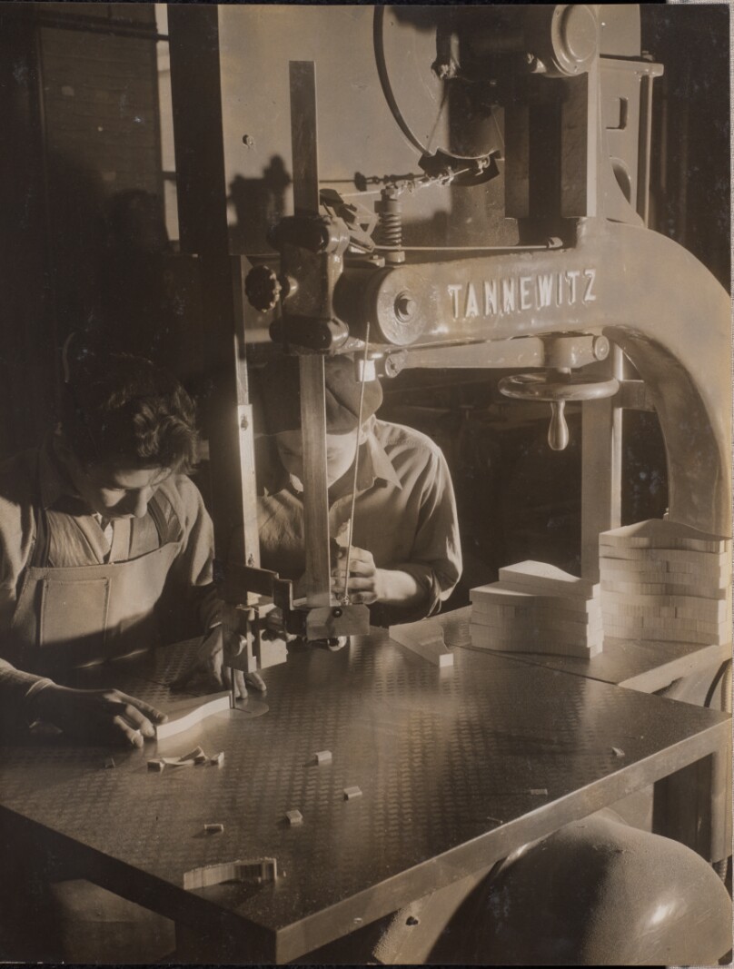 [Two men work with a band saw]