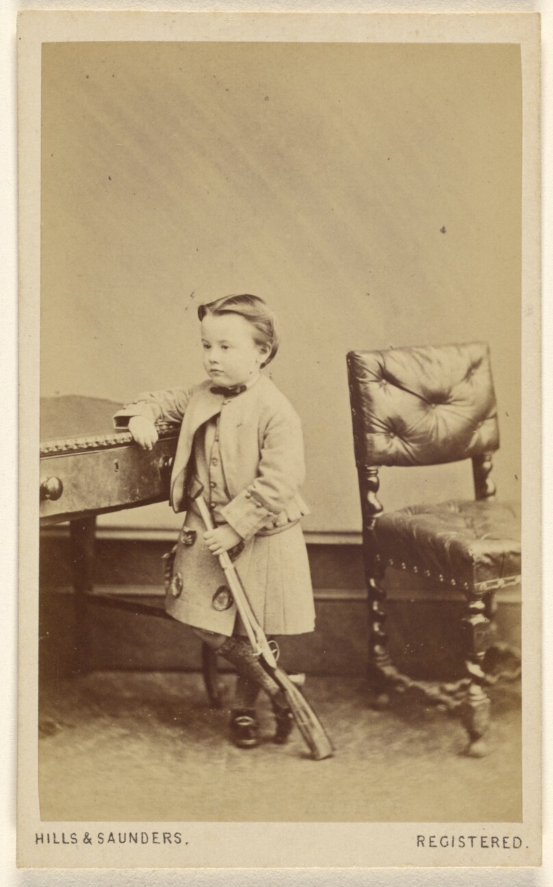 [Unidentified little boy standing, holding a toy rifle]