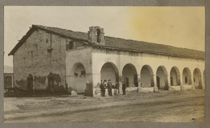 [Adobe building with arcade, men standing in front]