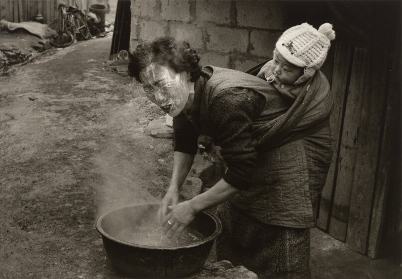 [Woman Washing Her Face While Carrying a Small Child on Her Back]
