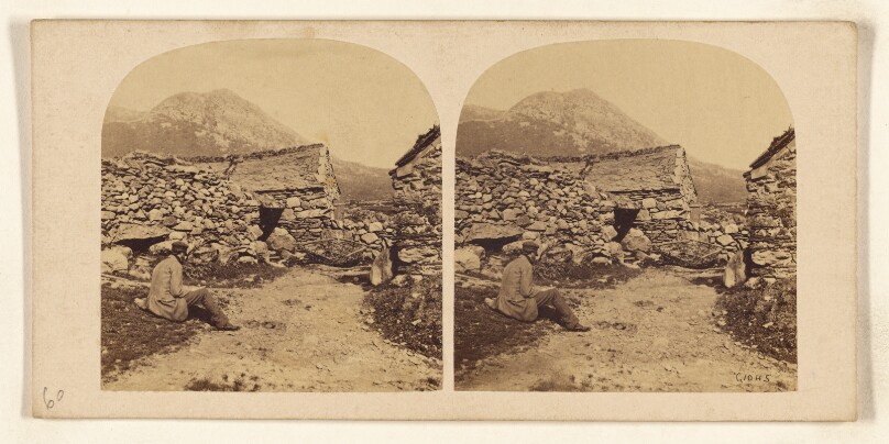 [Man seated on road near buildings made of stones]