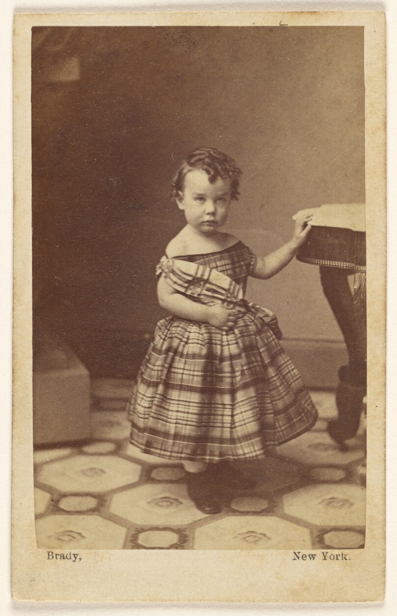 [Young girl standing with hand on table]
