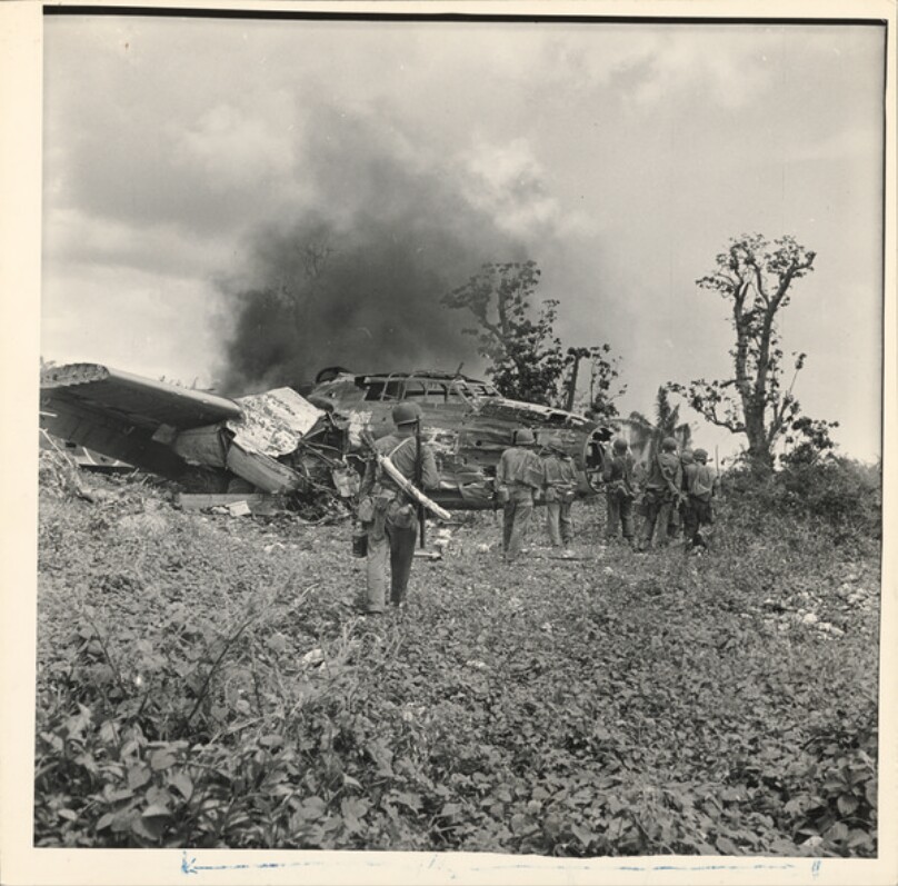 American soldiers near smoking, downed aircraft during WWII action on Orote Peninsula