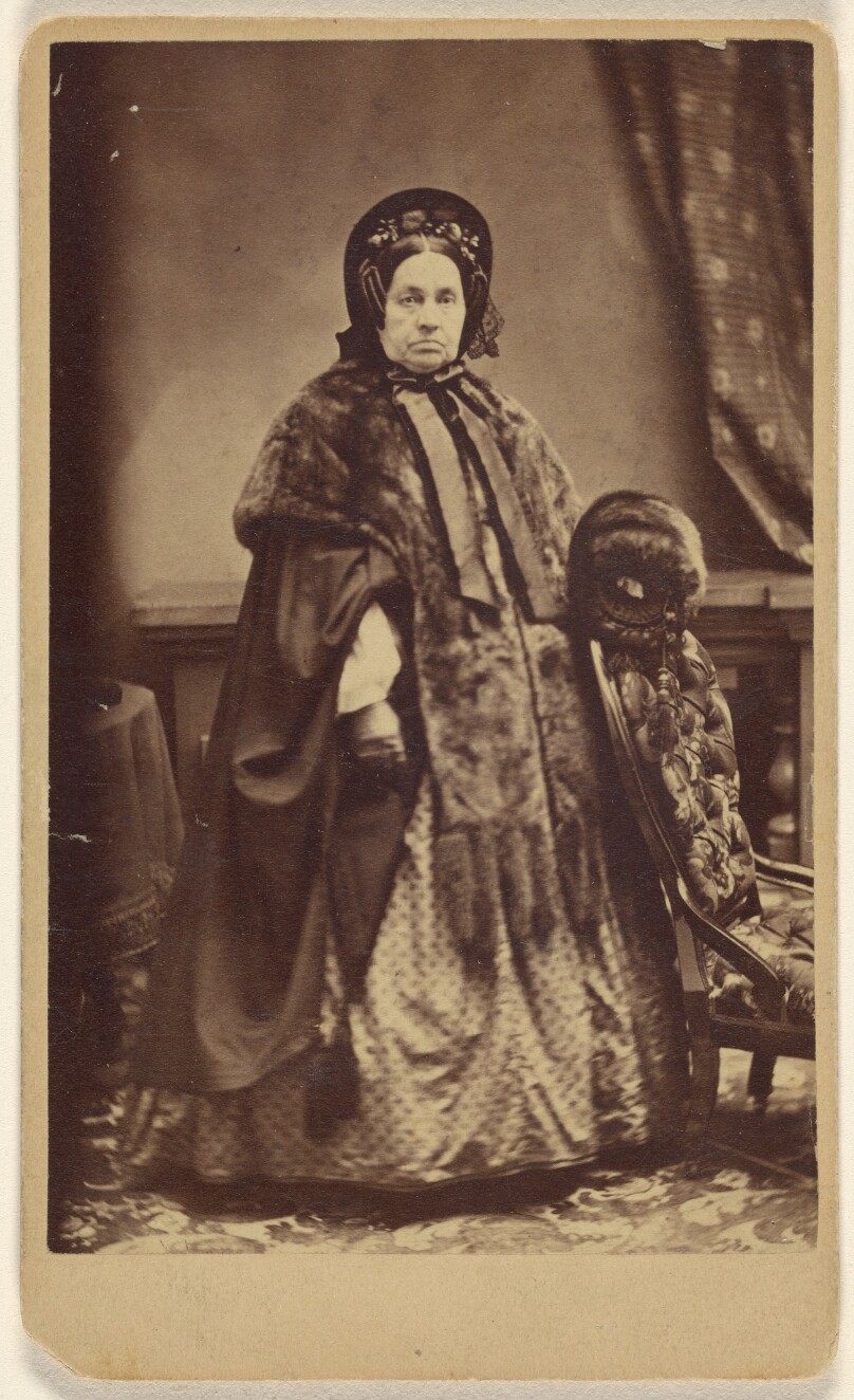 [Unidentified elderly woman wearing a fur coat and hat, standing]