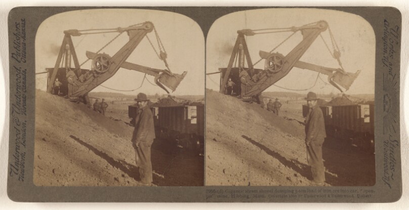 Gigantic steam shovel dumping 5-ton load of iron ore into car, "open-pit" mine, Hibbing, Minn.