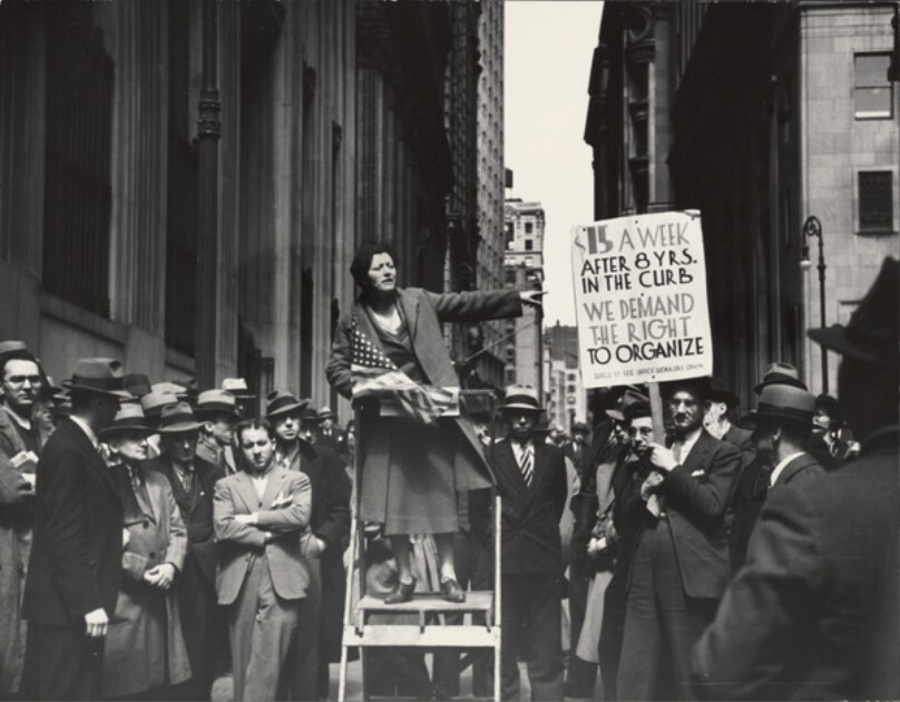 A pioneer organizer of the Office Worker's Union exhorts a crowd of sympathizers, Wall and Broad Sts., NYC