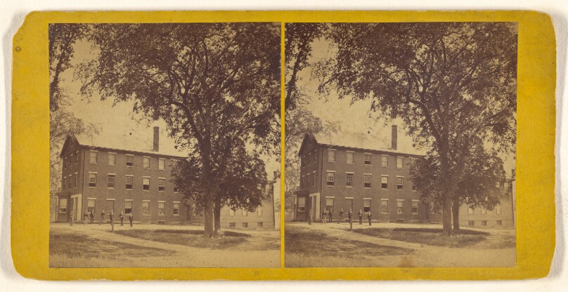 [View of a large building with men standing outside, possibly a college dormitory]