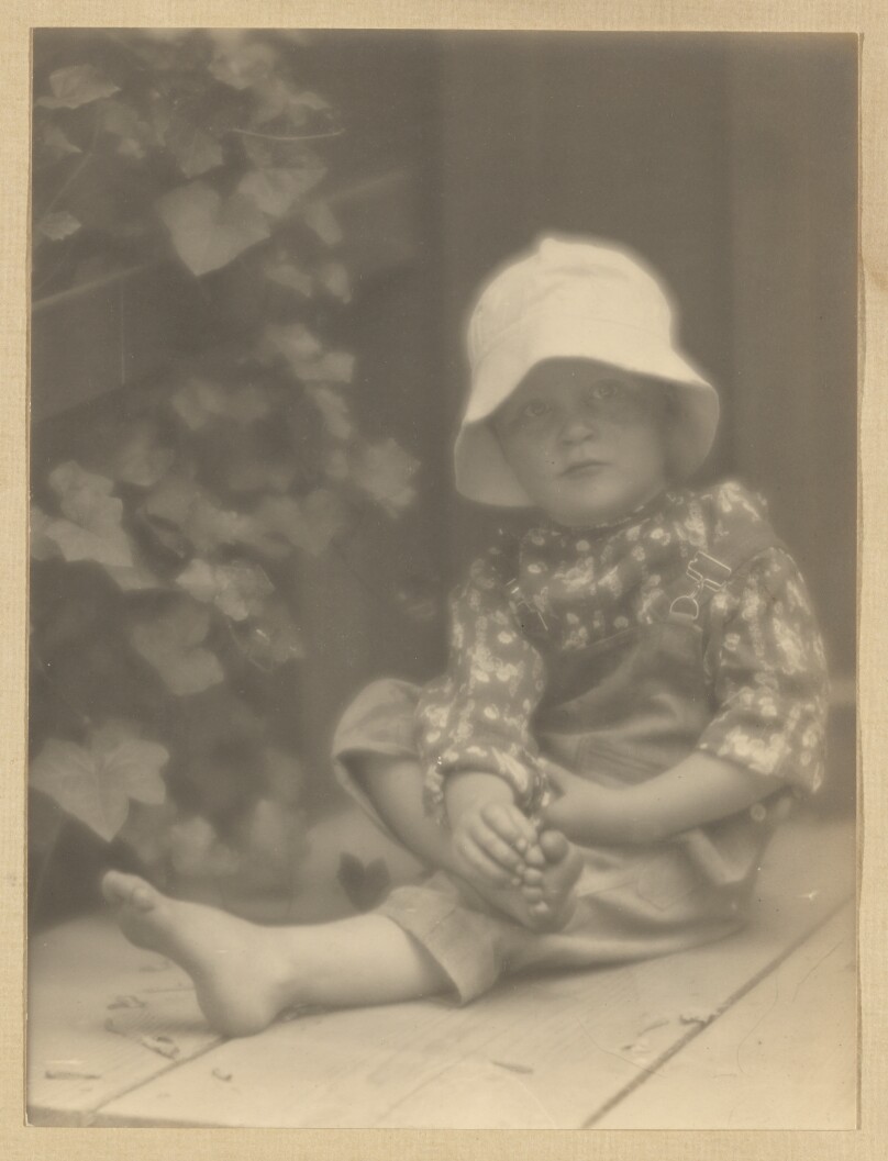 [Brett Weston, in overalls, seated, holding foot]