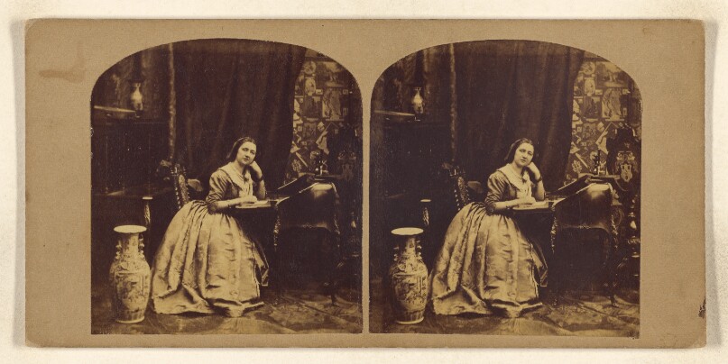 [Woman seated at writing table, hand on open book]