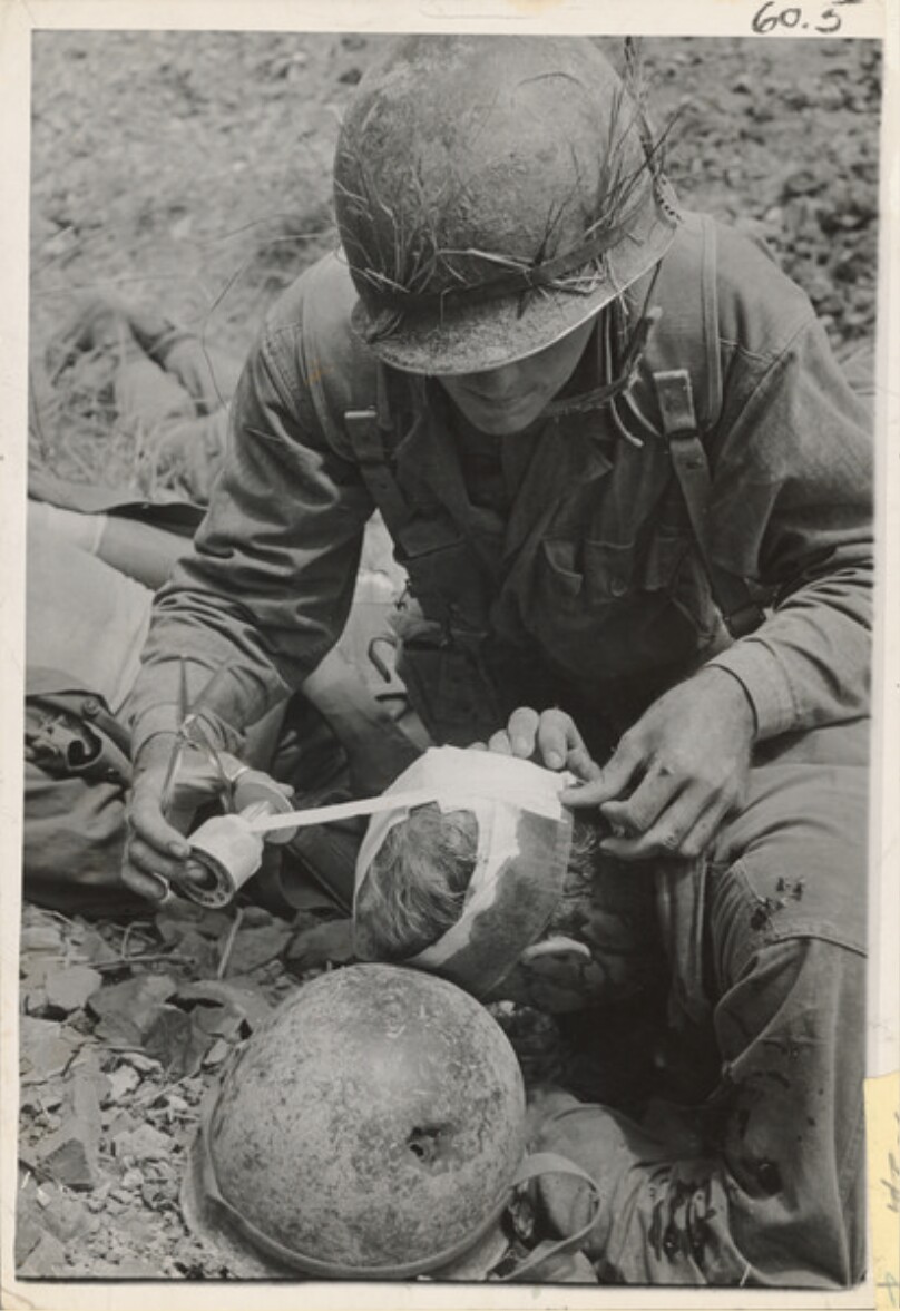 A soldier is wounded in back of head and the medic puts on an emergency bandage, Japan