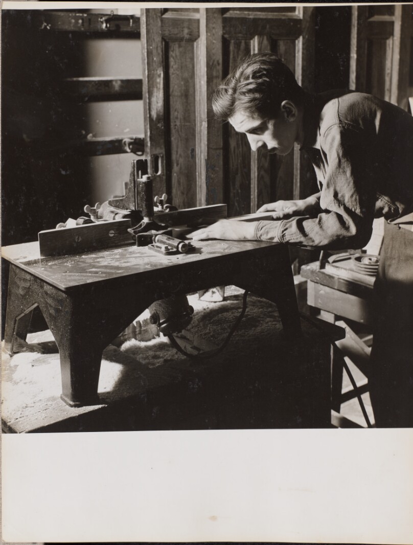 [Young man leans over a woodworking bench]