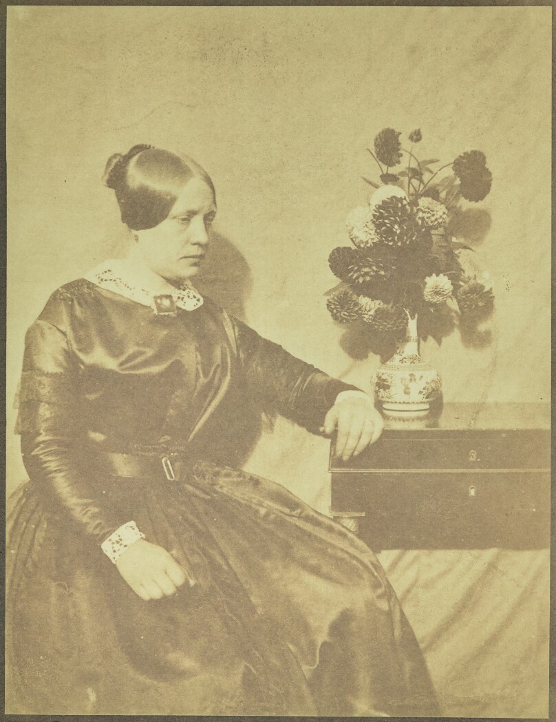 [Portrait of a Woman Seated beside a Table with Flowers]