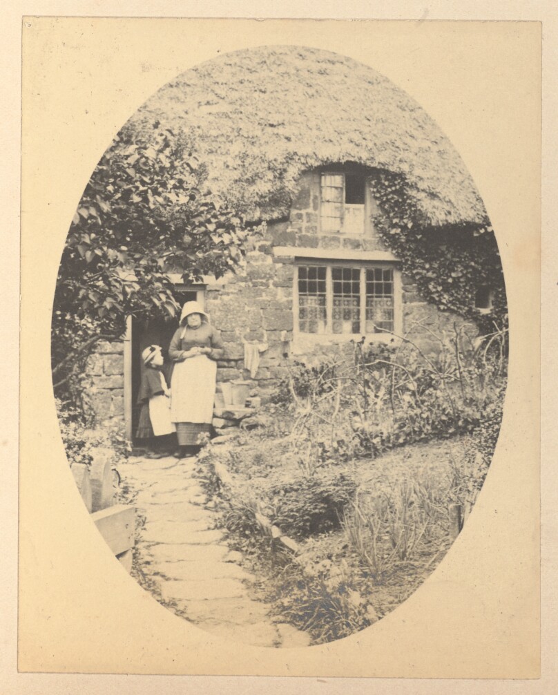 [Woman and child stand in front of a house]