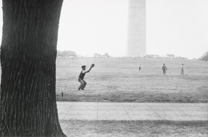 In spacious Washington, young men play in front of the George Washington Memorial after working hours.
