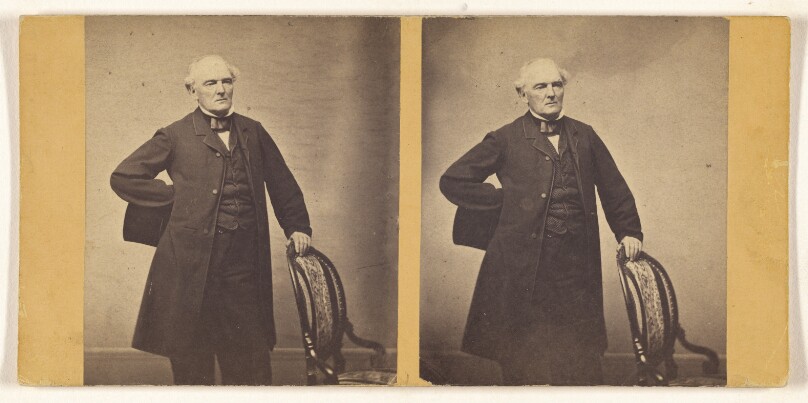 [Unidentified man standing, holding chair back and top hat]