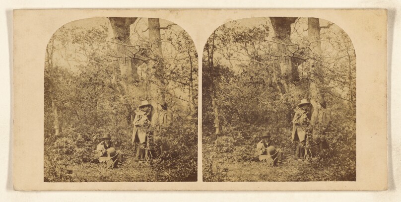 [Three men in the woods, all with hats, two standing, one seated]
