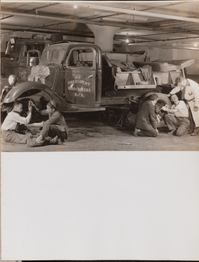 [Two groups of young men work on the wheels of a truck]