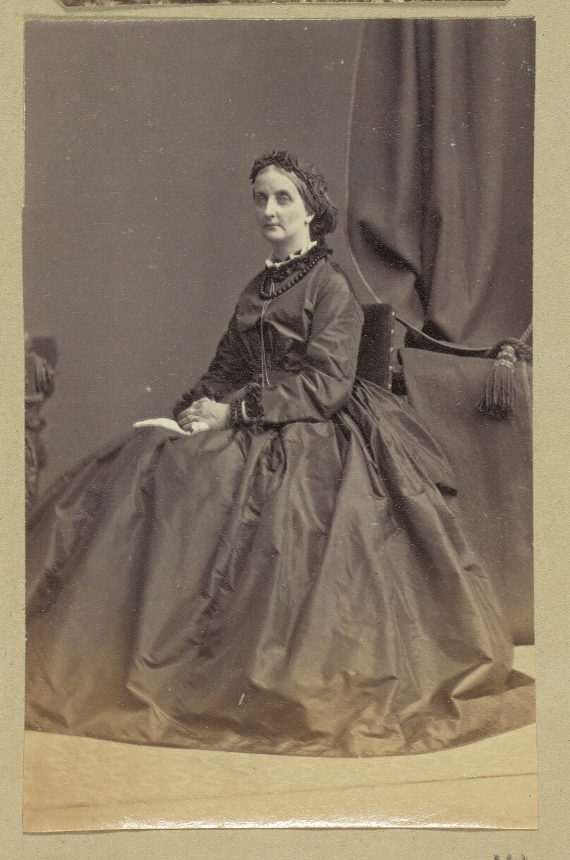 [Portrait of woman standing next to table and plant]