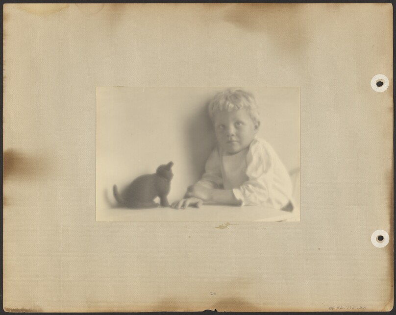 [Brett Weston in white tunic, playing with black rubber cat]