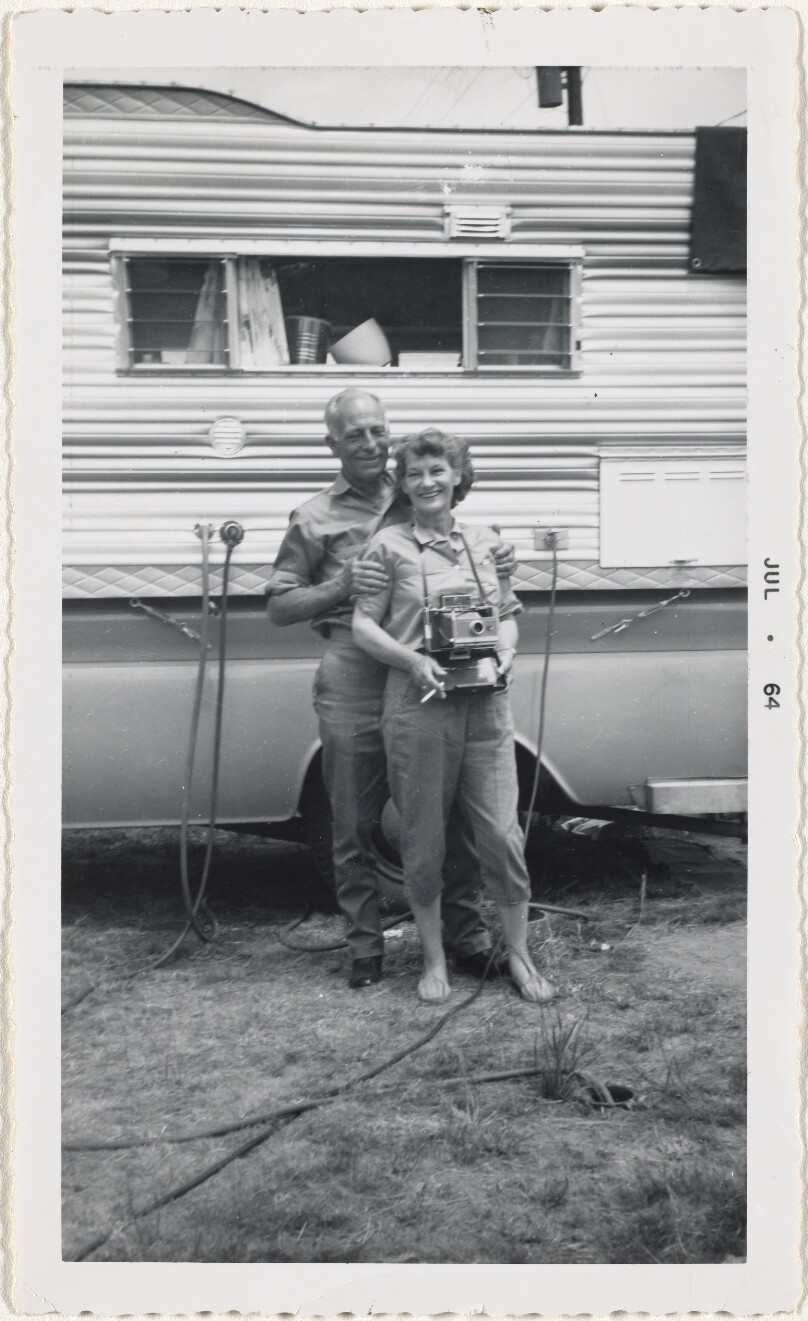 [Couple with camera in front of camper]