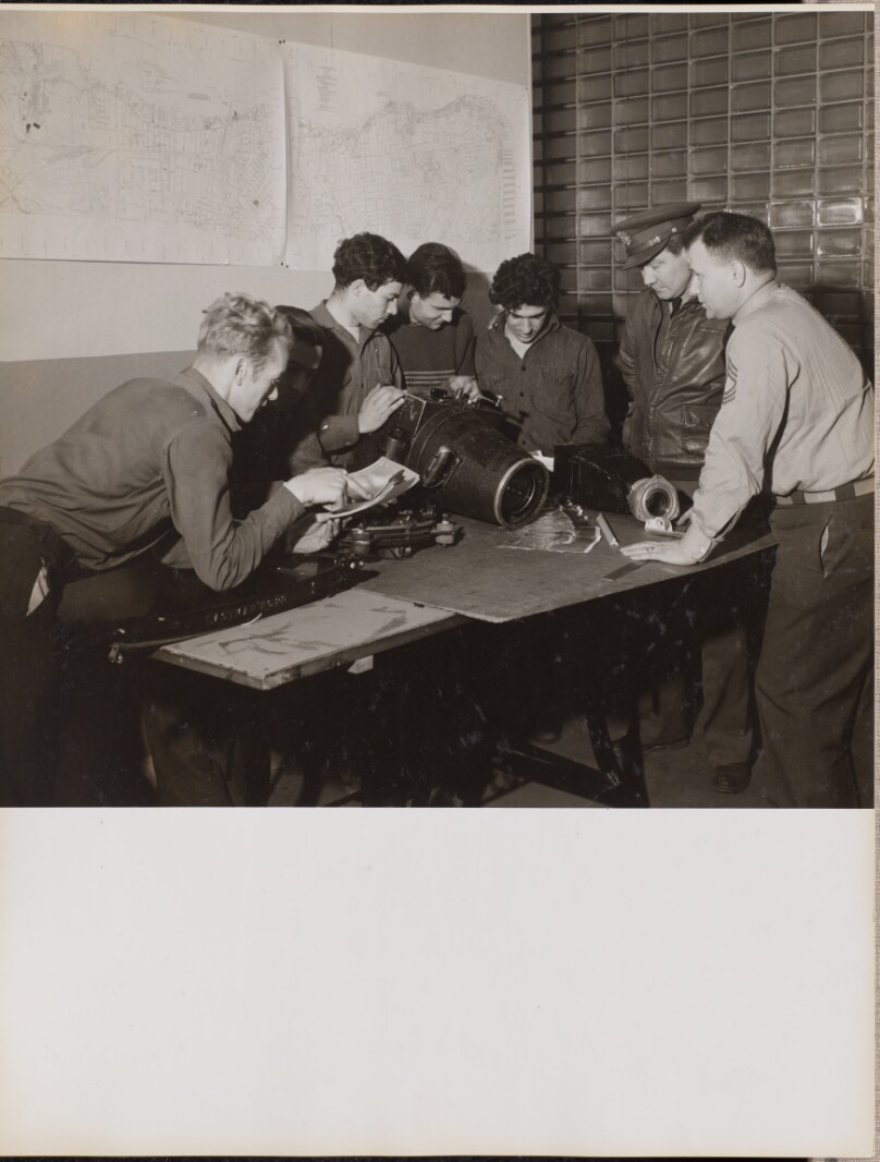 [Six men inspect a large camera]