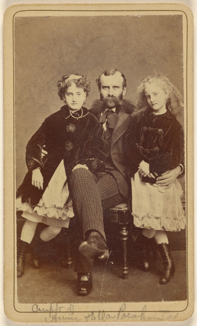 [Unidentified bearded man with two unidentified girls, all seated in the same chair]