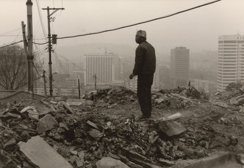 [Grey-Haired Man Standing on Rubble on a Hill Overlooking Seoul]
