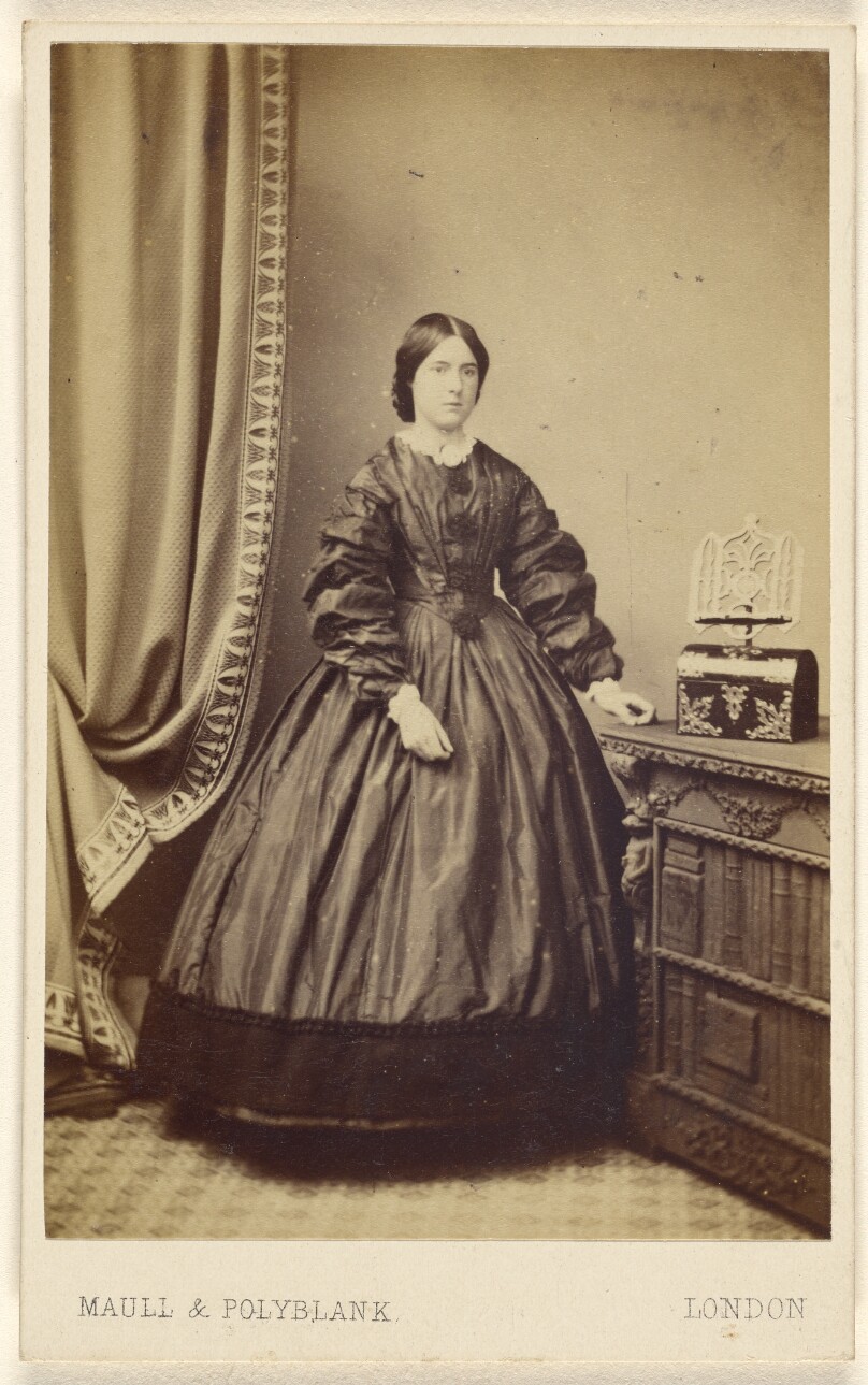 [Unidentified woman wearing a long dress, standing]