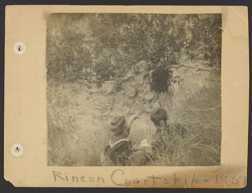 [Flora and Edward Weston sitting on grass, Flora pointing to cliff]